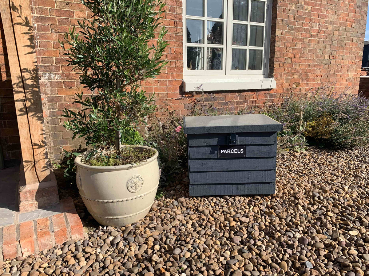 Dark Grey DelSafe wooden parcel delivery box beside a doorway and garden planter