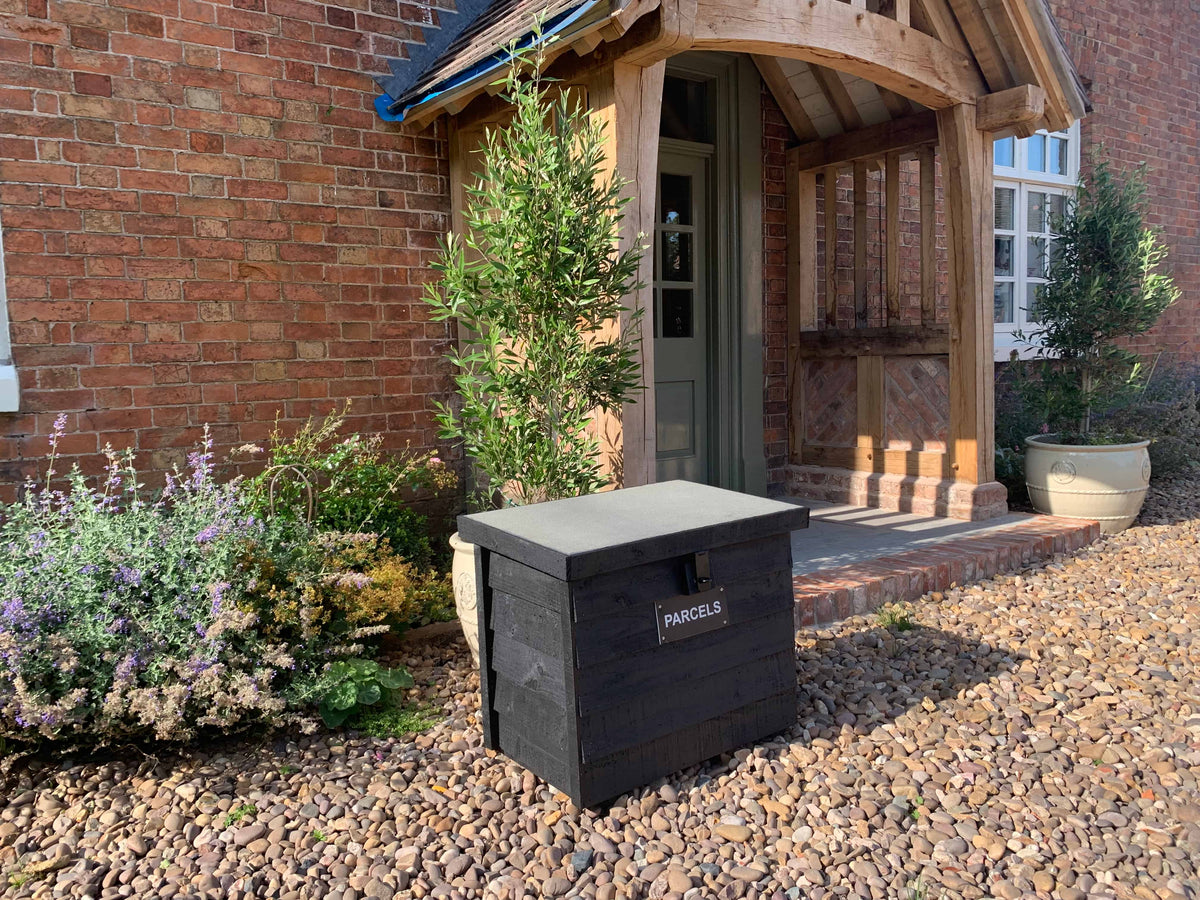 Black DelSafe wooden parcel delivery box beside a timber garden porch