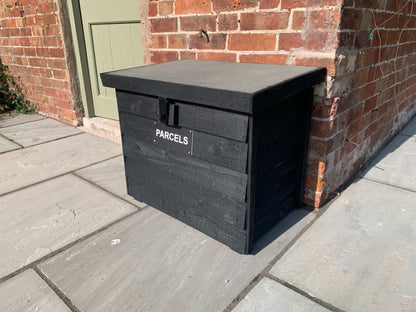 Black DelSafe wooden parcel delivery box with grey felt roof beside a brick wall