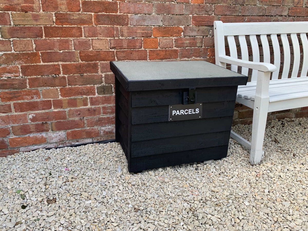 Black DelSafe wooden parcel delivery box beside an outdoor seating area